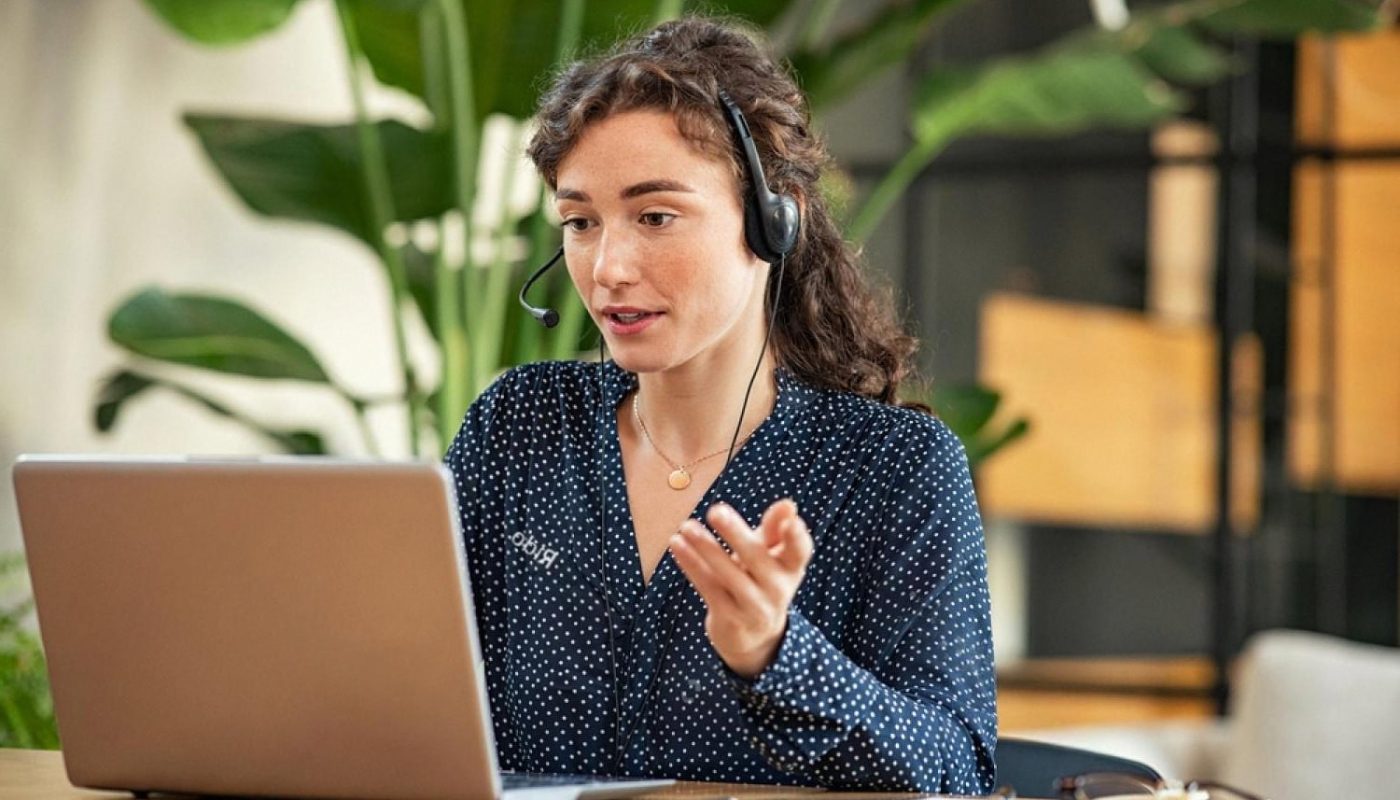 Customer service agent wearing a headset helping a client on a laptop, representing modern queue and support management