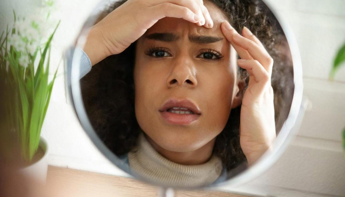 Young woman in the UAE checking acne breakouts on her forehead in a mirror