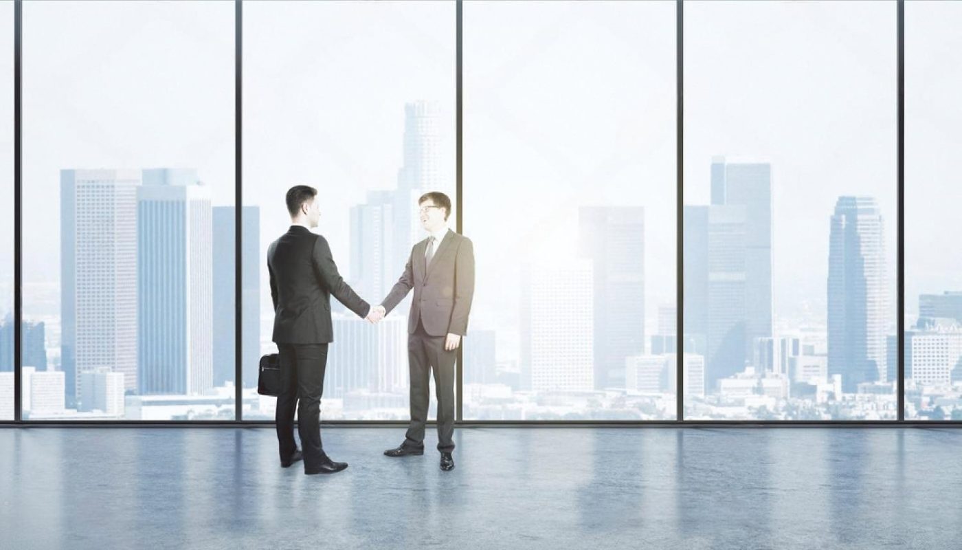 Two businessmen shaking hands in a modern office overlooking a city skyline